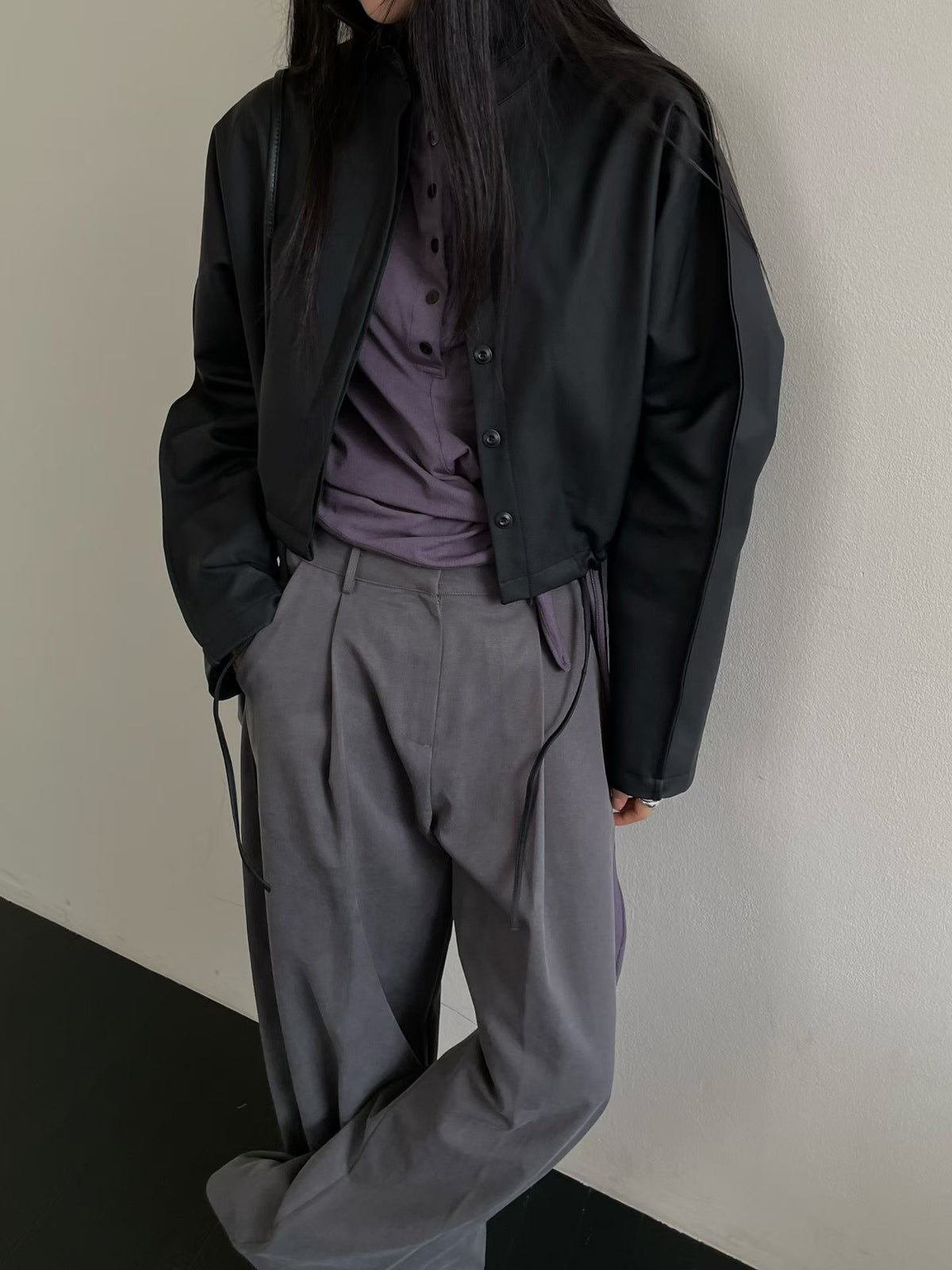 Black button-front faux leather jacket worn open over a purple top with grey trousers