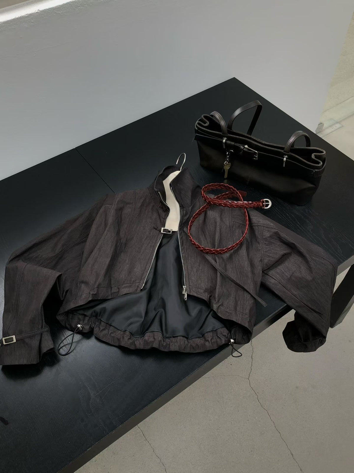 Charcoal bolero jacket laid open on a black table, showing lining and hem drawstrings