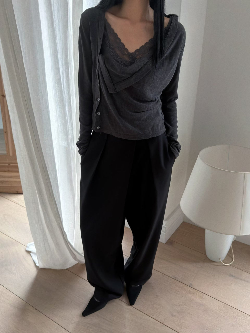 Charcoal long sleeve cardigan with a draped front and asymmetric buttons worn over a lace-trim top.
