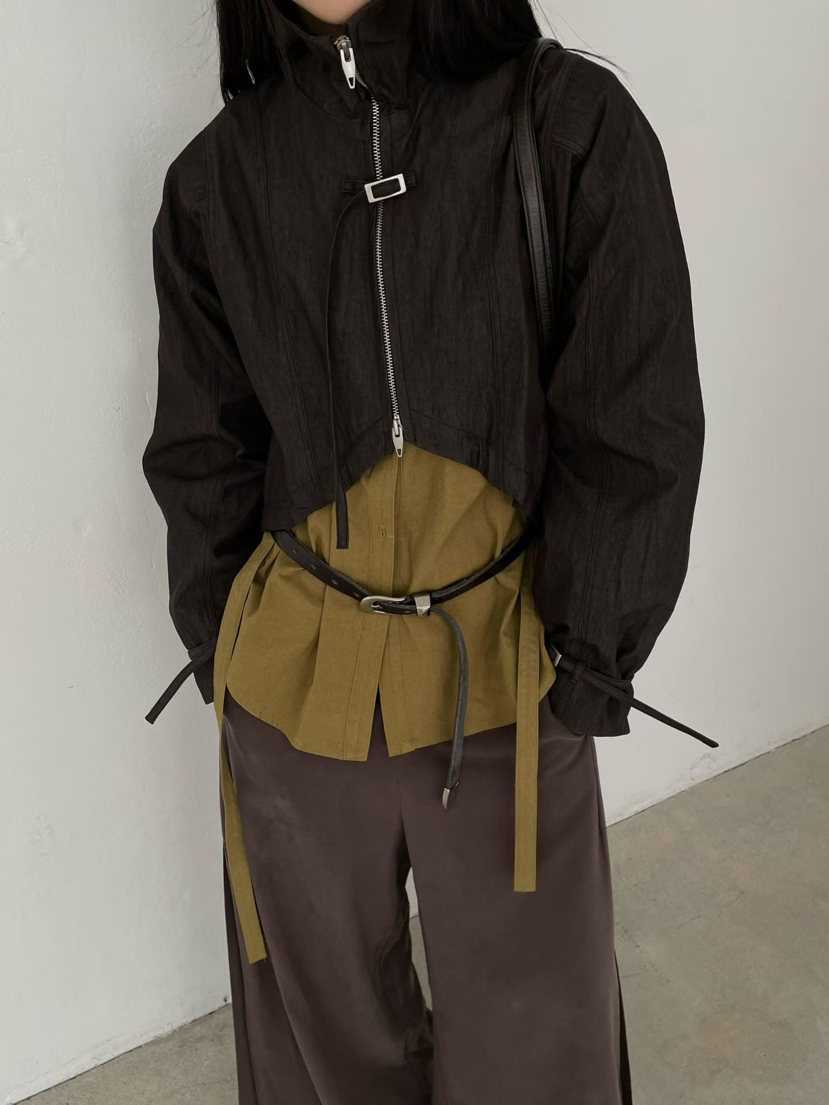 Black cropped zip-up bolero jacket with front buckle, layered over a khaki shirt