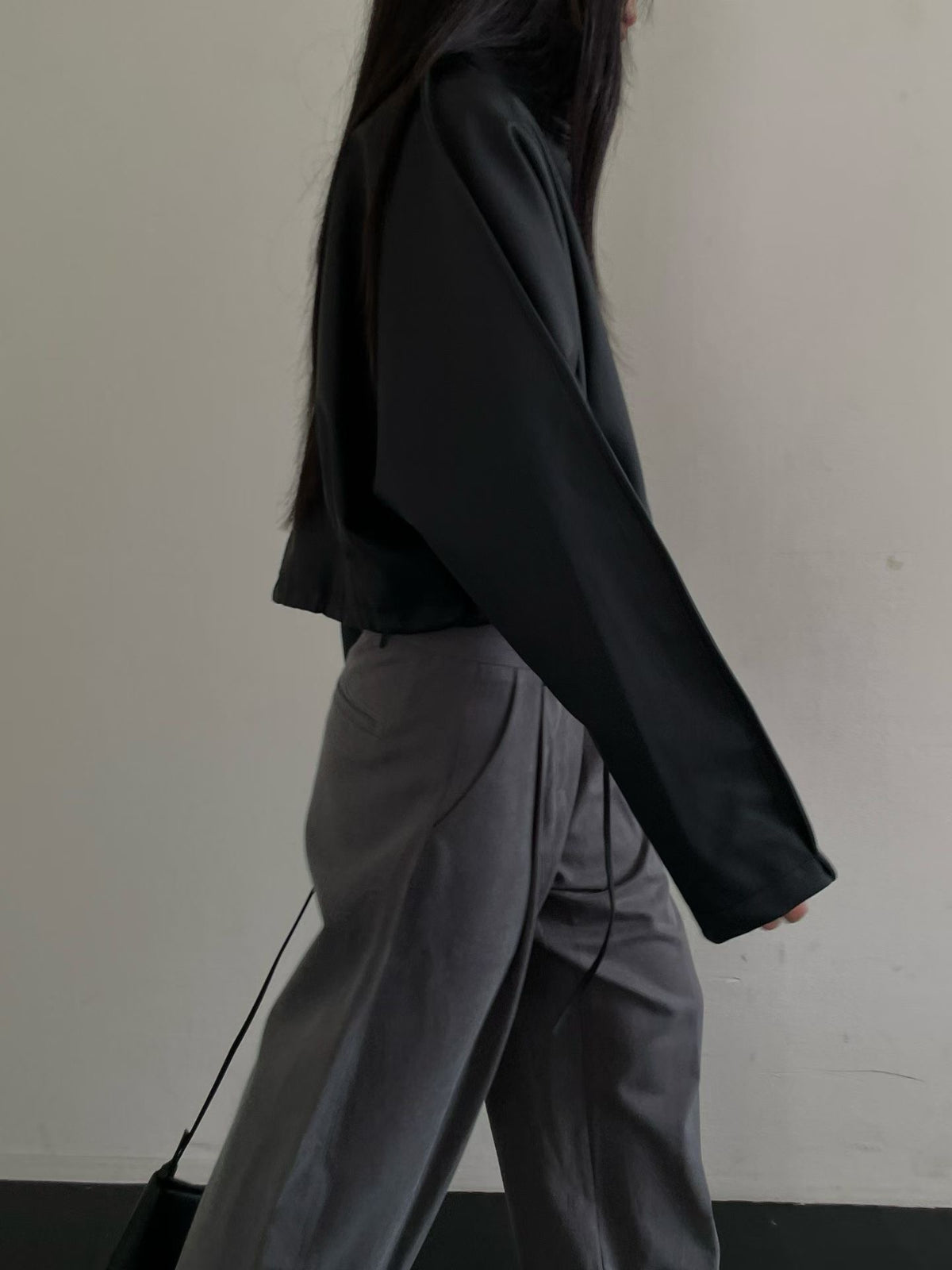 Side view of black cropped faux leather jacket with long sleeves, styled with grey trousers