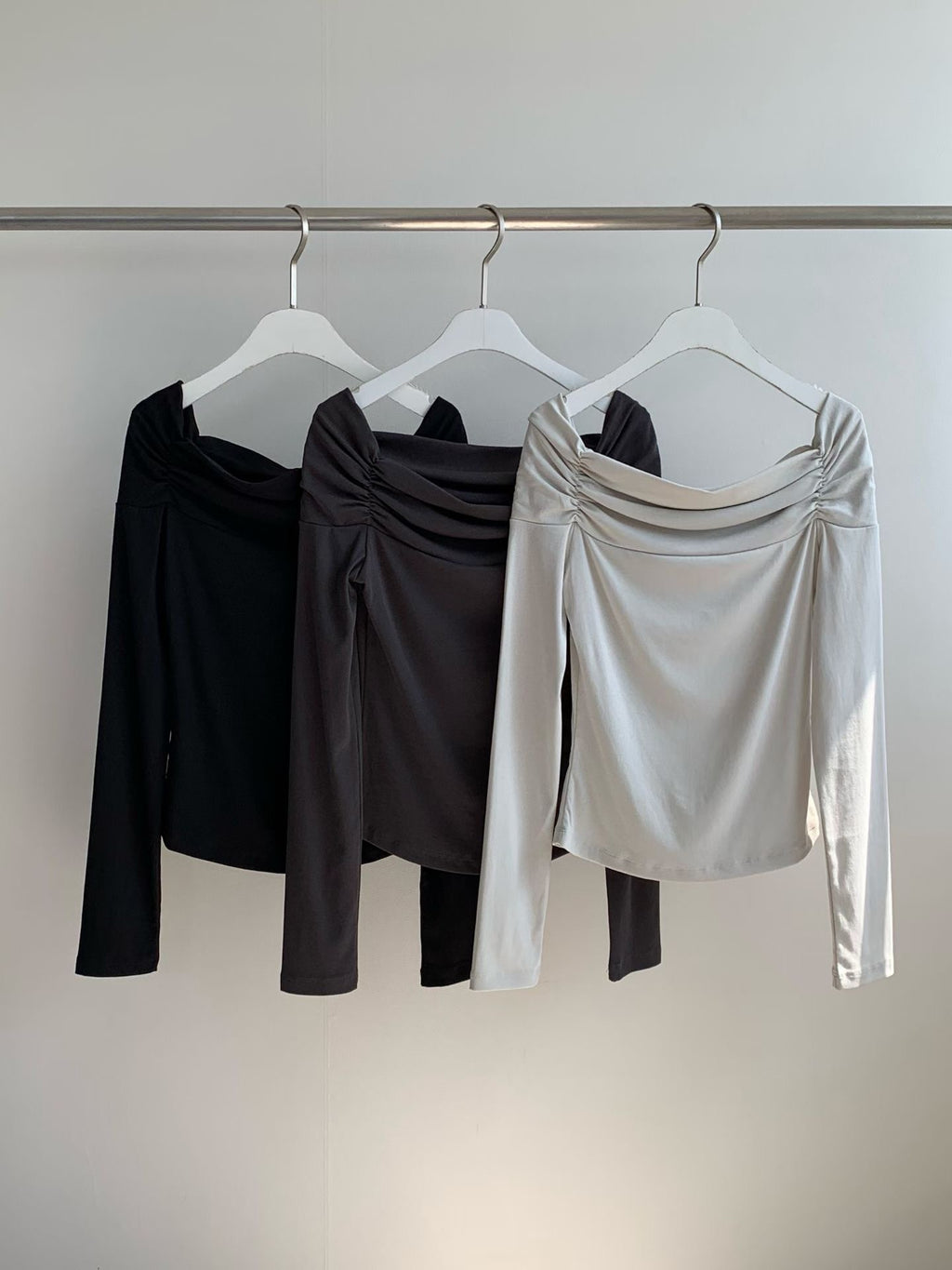 Charcoal ruched off-shoulder top worn with crossed arms and a white lace-hem skirt.