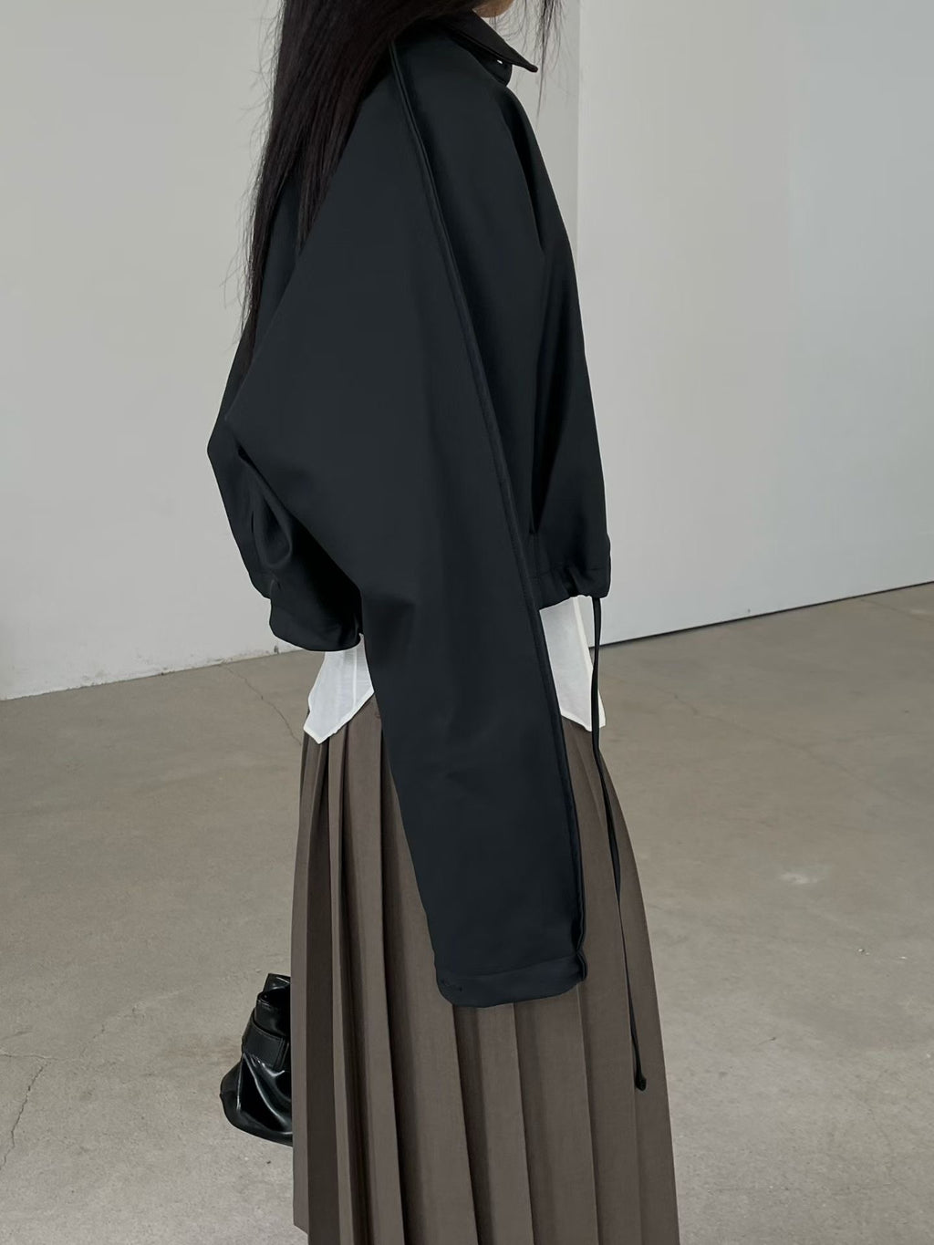 Side view of black collared faux leather jacket styled with a brown pleated skirt