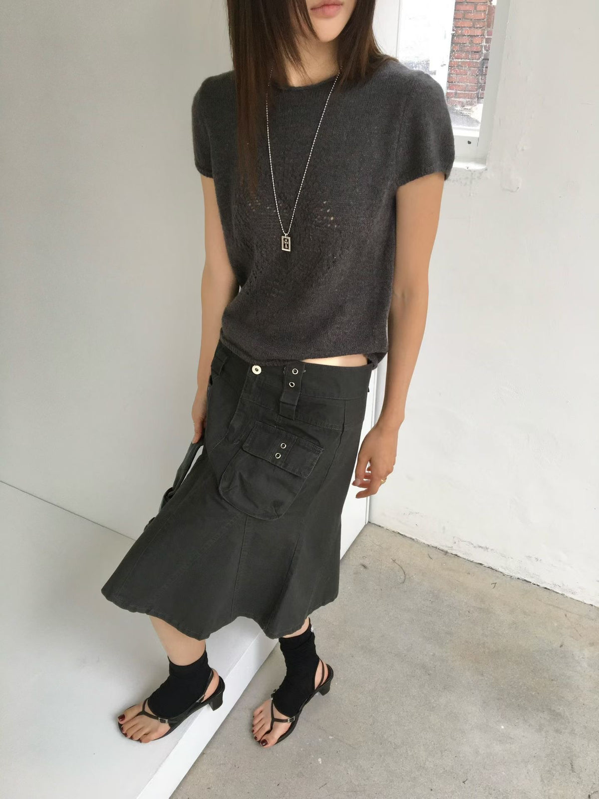 Close-up of a charcoal A-line cargo skirt showing front pockets, eyelets and two waistband buttons.