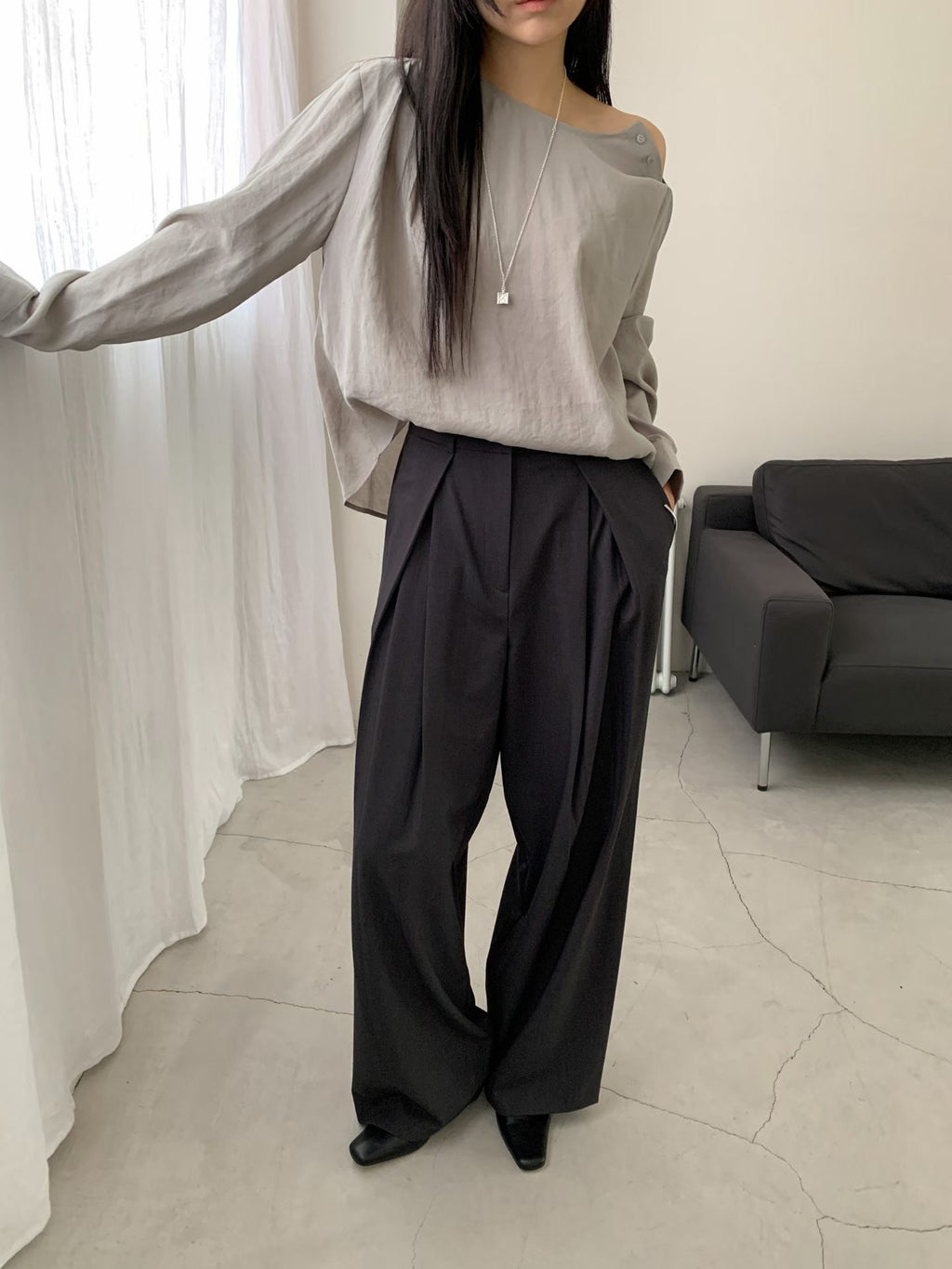 Seated woman wearing beige pleated wide leg pants with a brown blouse.
