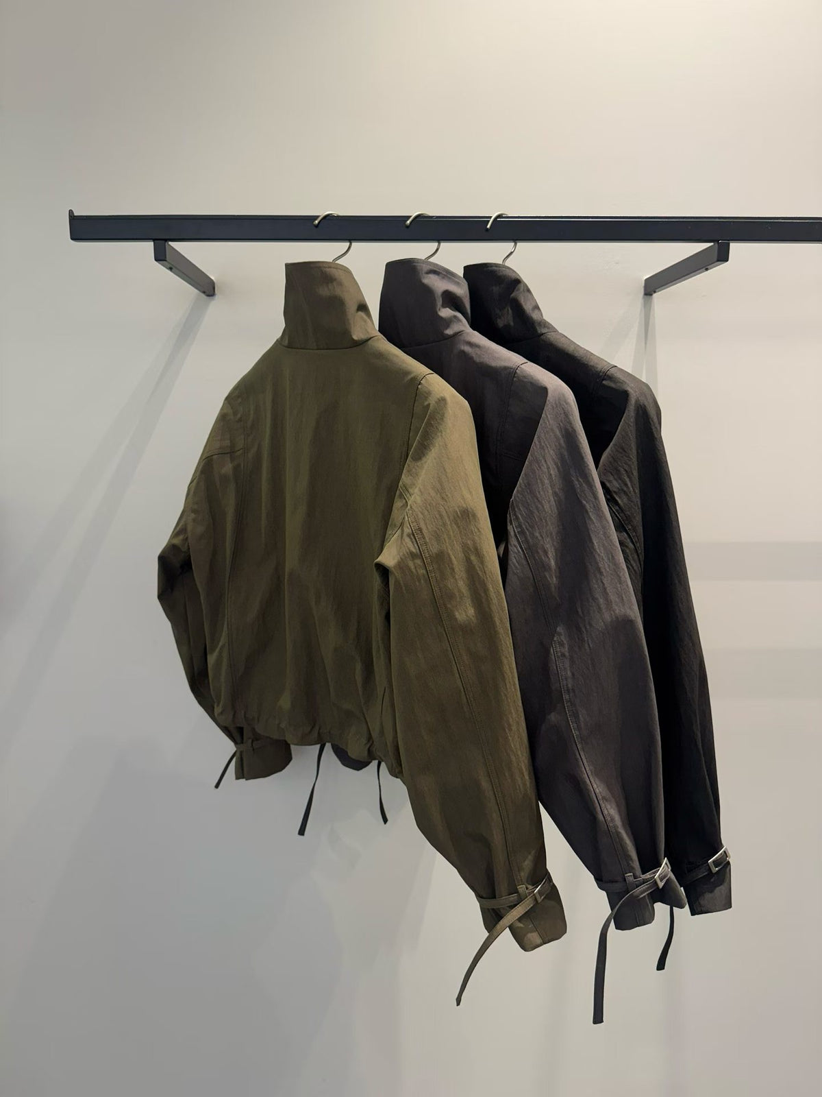 Back view of Khaki, Charcoal and Black bolero jackets on hangers with buckle cuffs