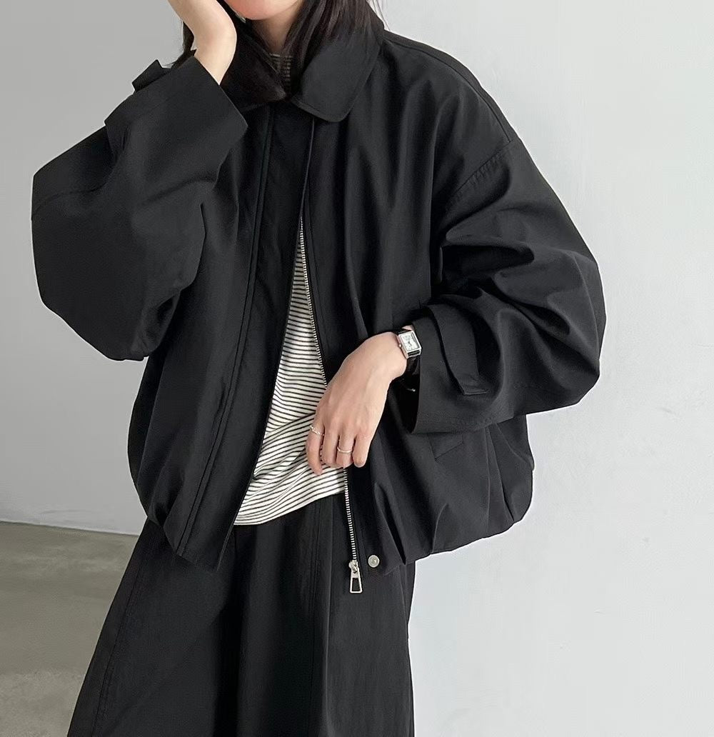 Woman wearing an ivory collared zip-up blouson jacket with dark trousers.