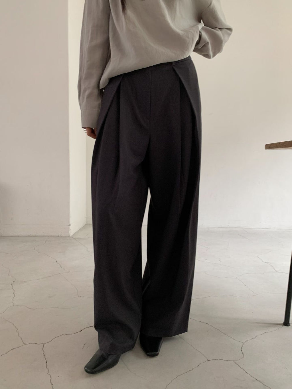 Full-length front view of charcoal pleated wide leg pants styled with a grey blouse.