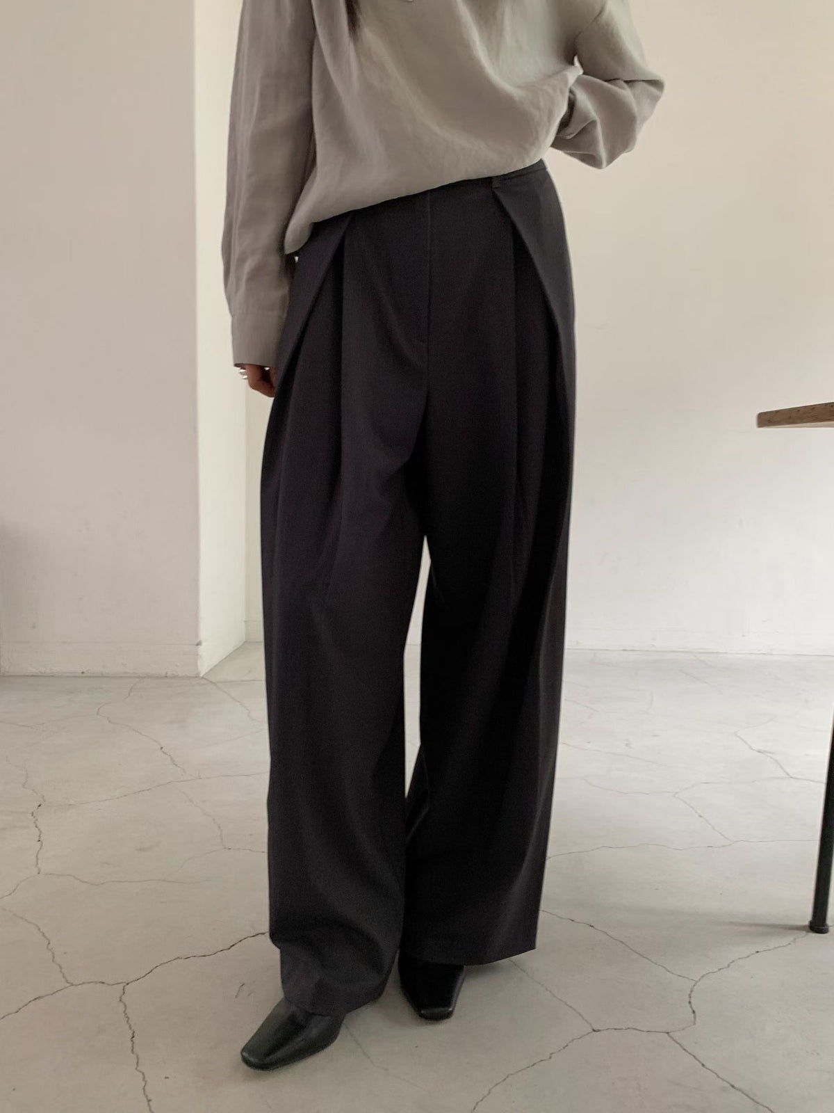 Full-length front view of charcoal pleated wide leg pants styled with a grey blouse.