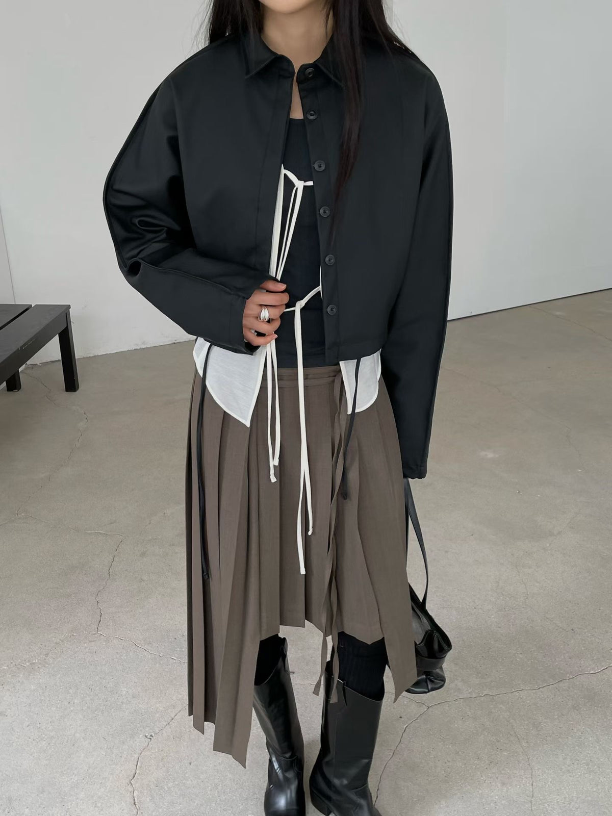 Women's black cropped faux leather jacket with collar and front buttons, styled with a pleated skirt