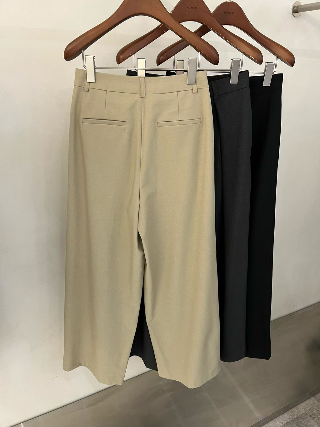 Chae pleated wide leg pants in Beige, Charcoal and Black on wooden hangers.