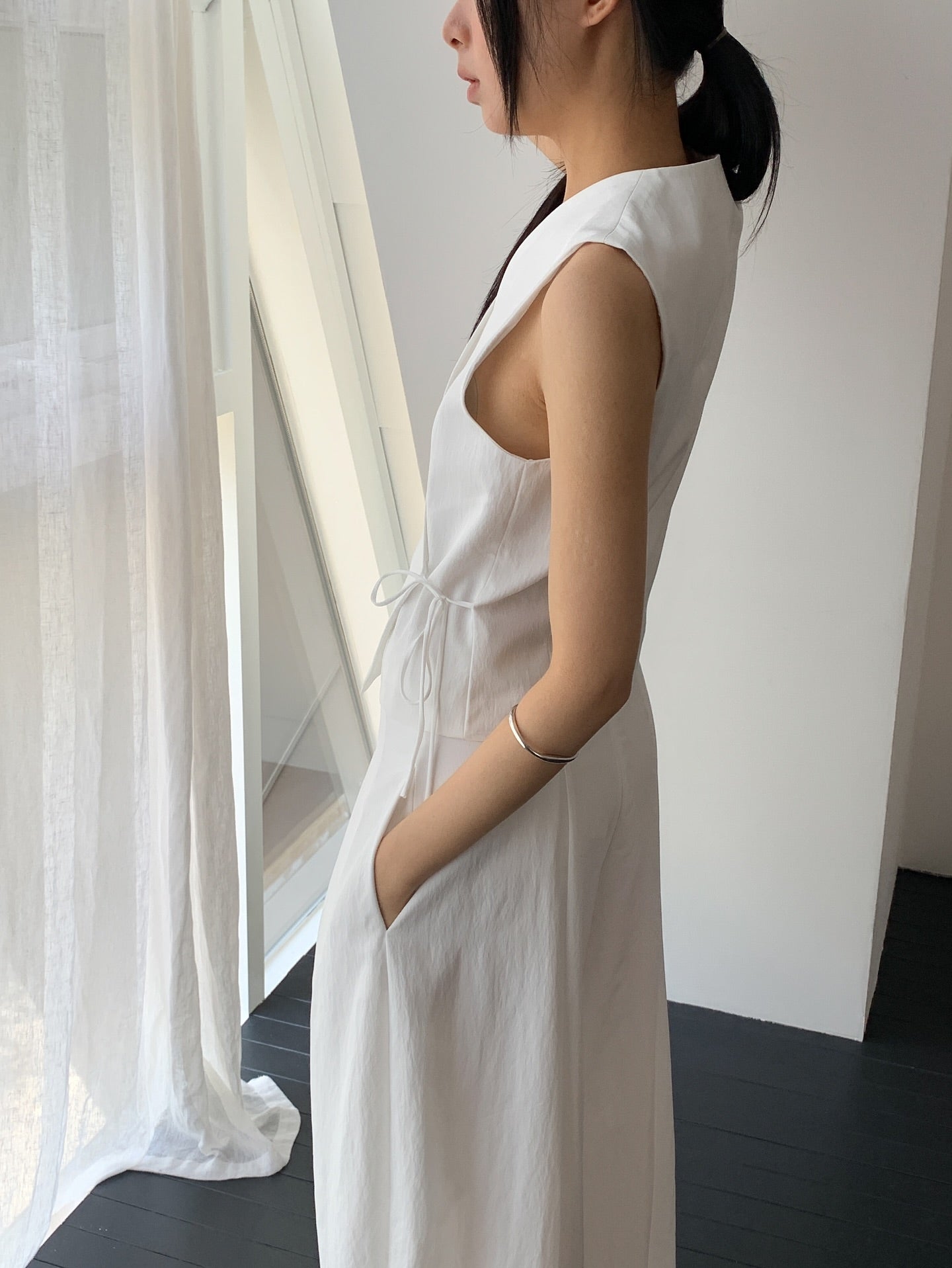 Vivel cross wrap vest in White, styled on model front view close-up tie string detail with white wide leg pants