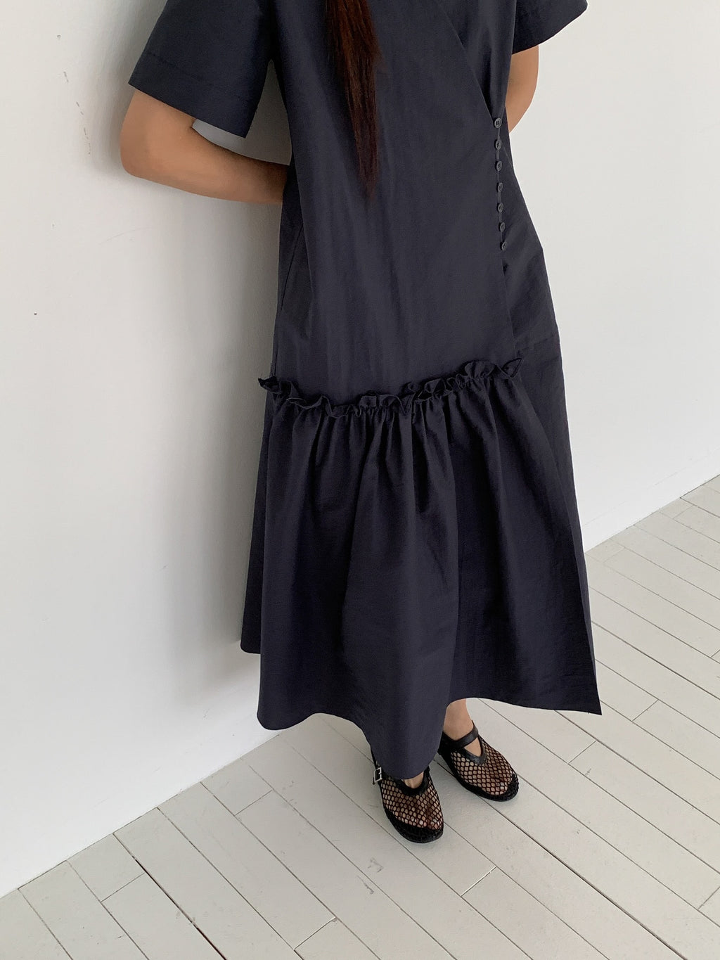 Vivel wrap shirring maxi dress in Charcoal, styled on model front view close-up button and shirring detail leaning on wall