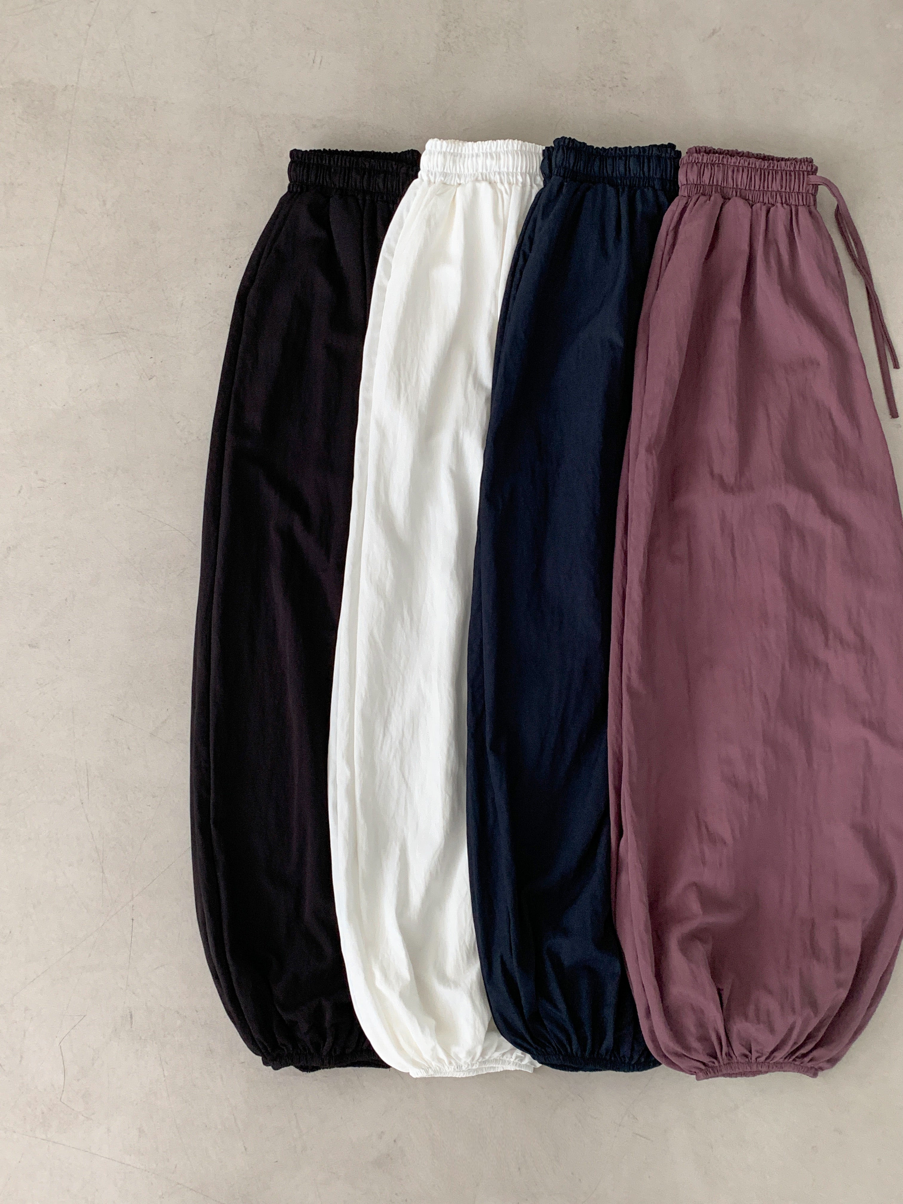 Merrymore drawstring elastic waist harem pants in Burgundy, styled on model front view with white crop top and black mini bag leaning on white wall