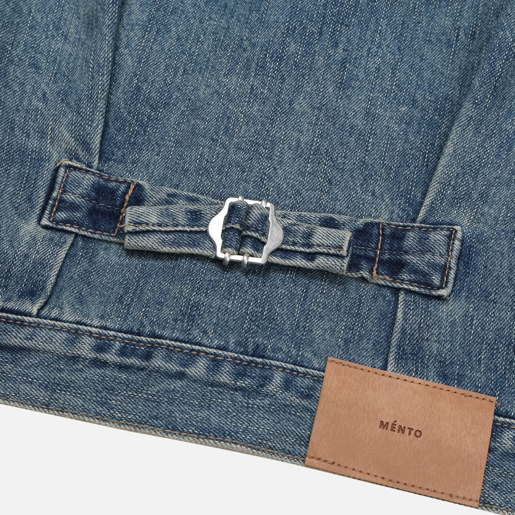 Metal button and waist adjustment detail on a mid-wash denim jacket