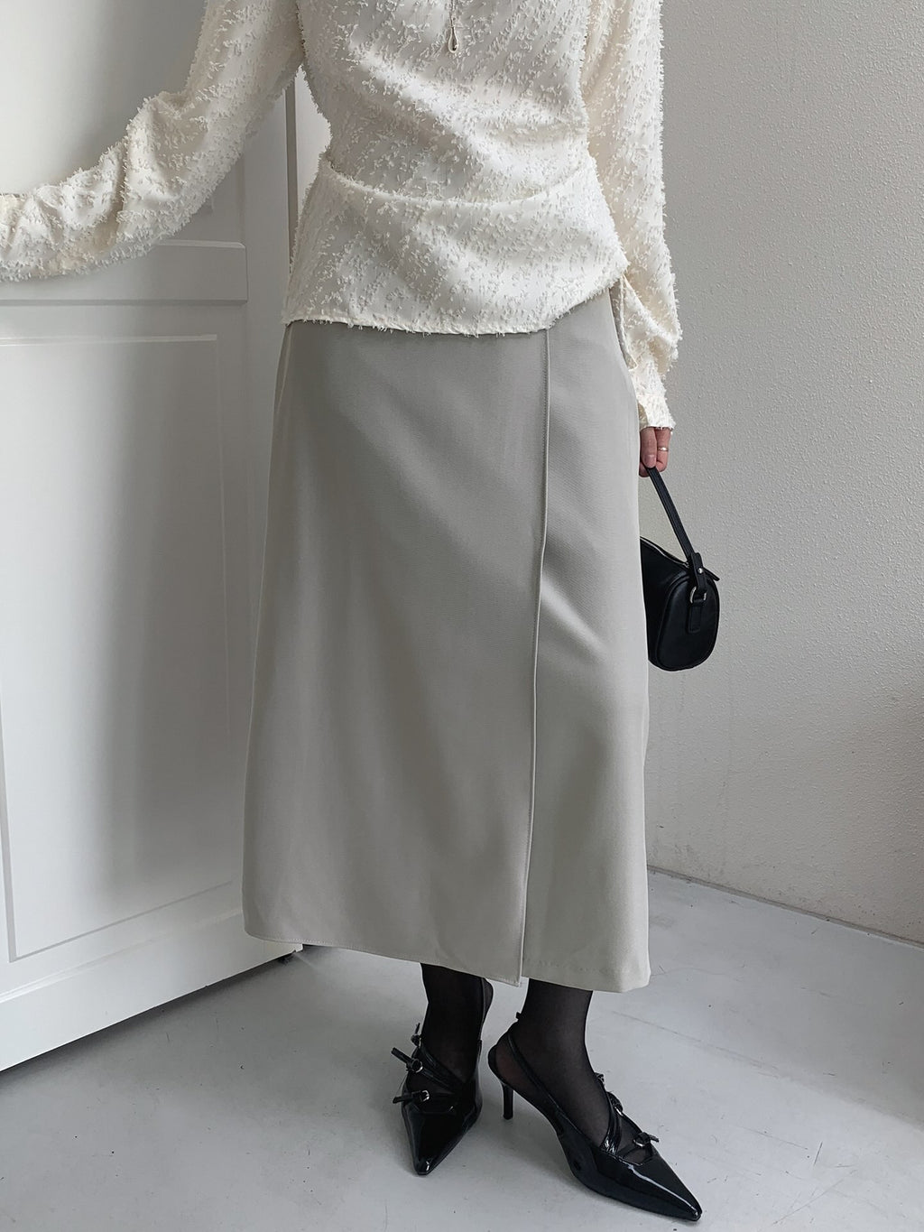Front view of a beige midi skirt showing its overlapping panel, worn with an ivory top.