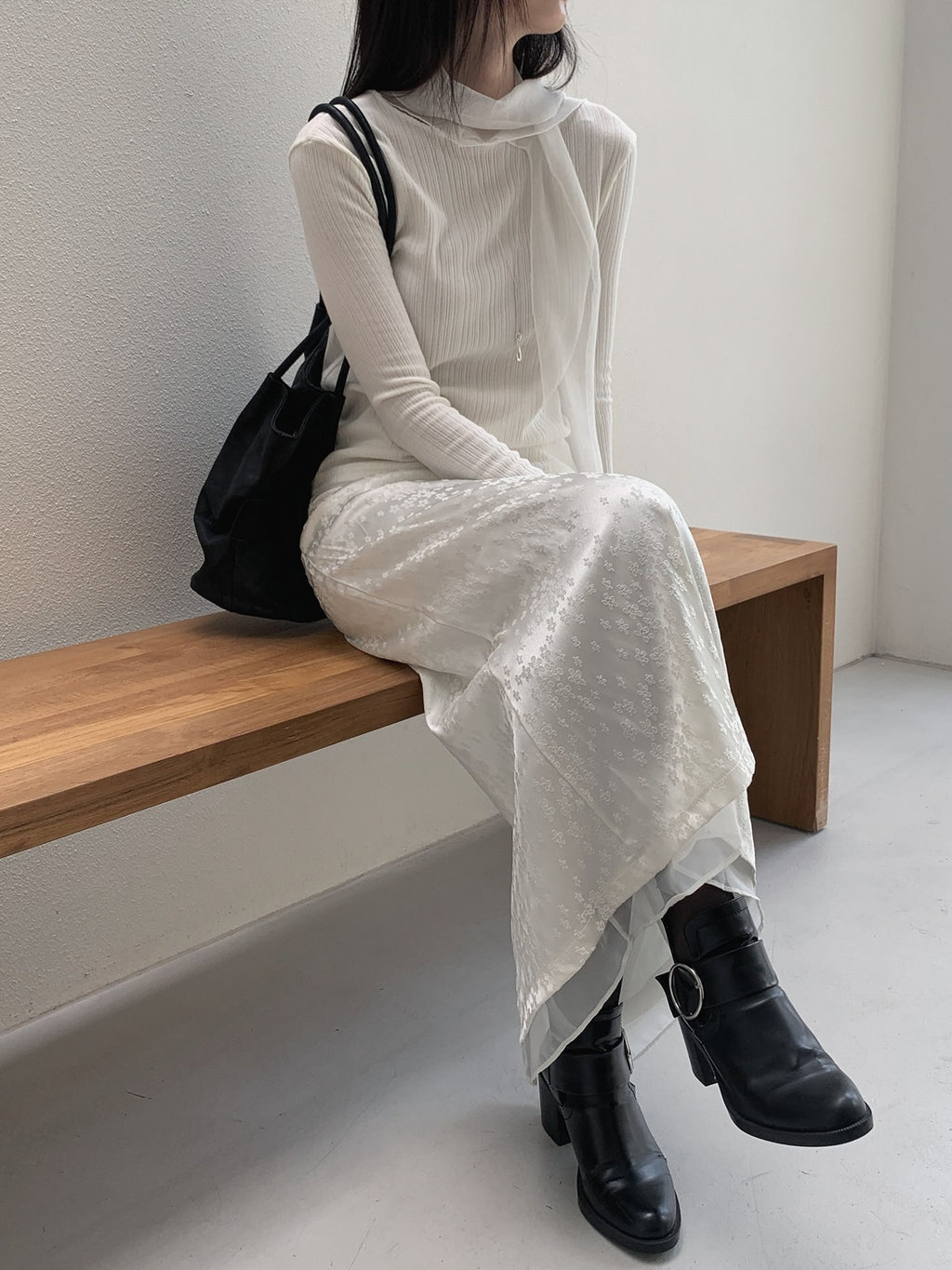 Seated front view of a cream ribbed long sleeve top with long neckline ties and a floral skirt.
