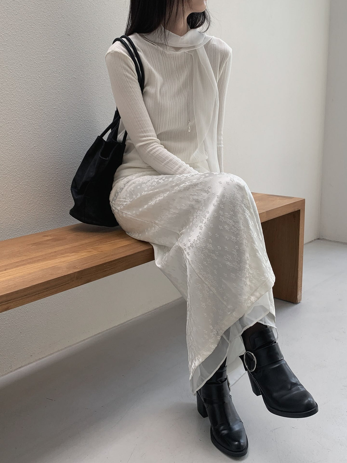 Seated front view of a cream ribbed long sleeve top with long neckline ties and a floral skirt.