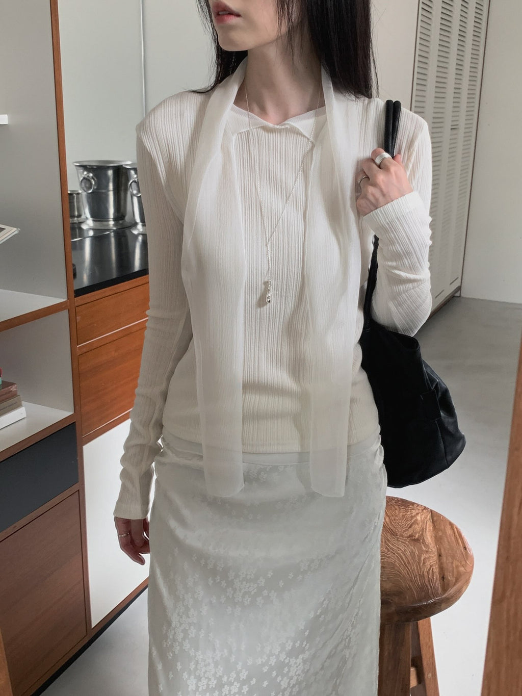 Cream, brown and black Rowsatnd ribbed tie-neck tops laid on a white bed.