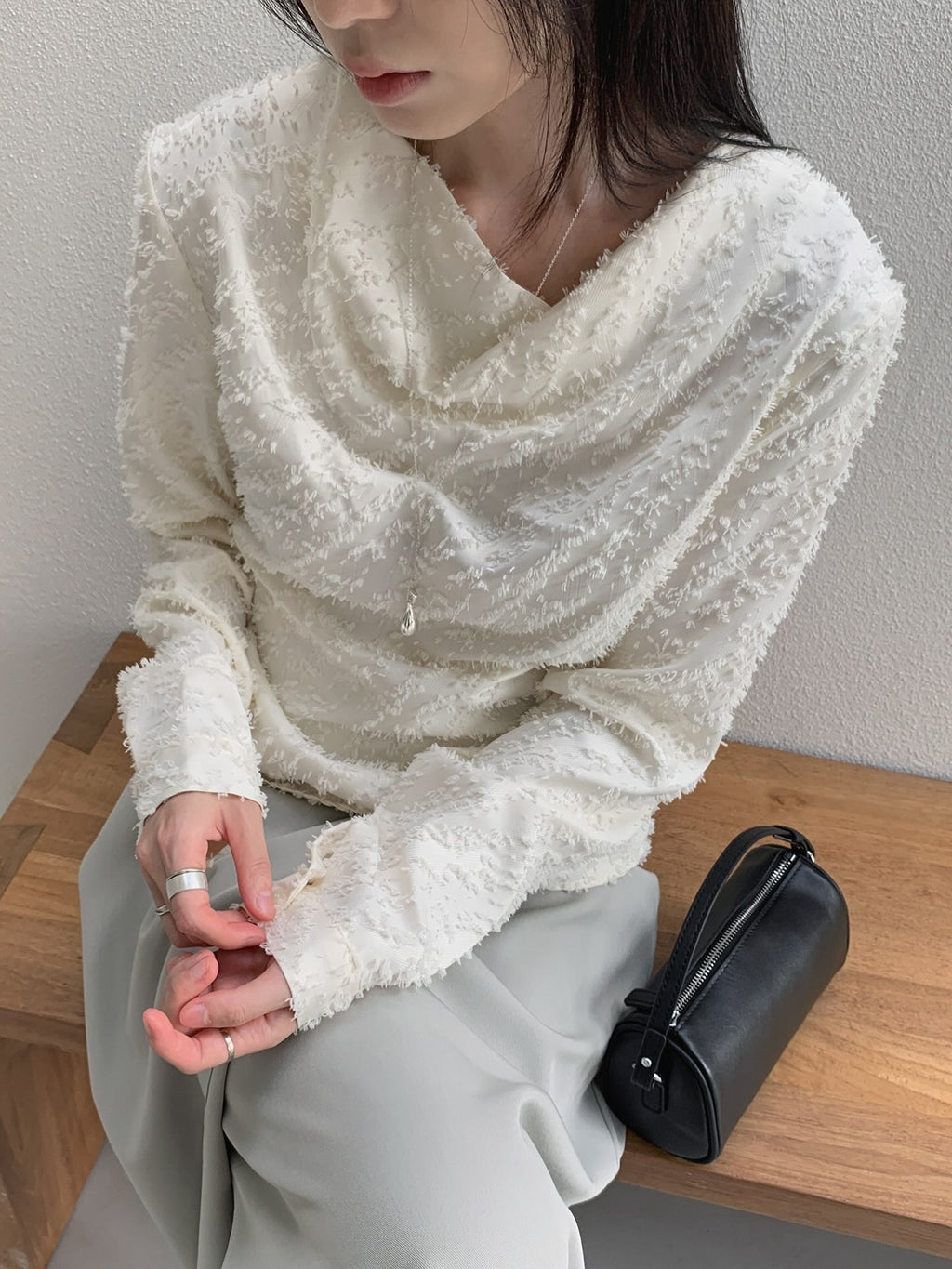 Seated front view of a cream cowl neck blouse styled with a light-coloured skirt.