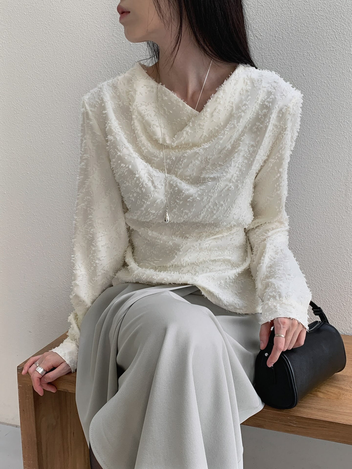 Rear side view of a cream long sleeve blouse showing textured fabric and a back waist bow.