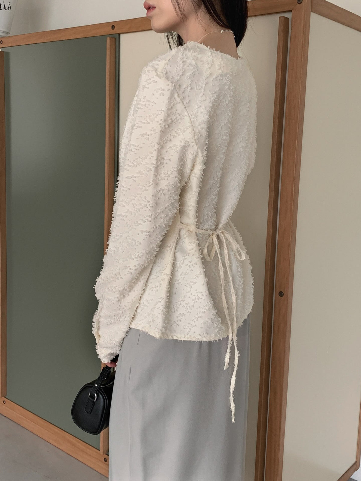Cream and black textured long sleeve cowl neck blouses on wooden hangers.