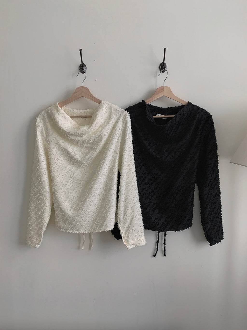 Black and cream textured blouses laid flat with their back waist ties visible.