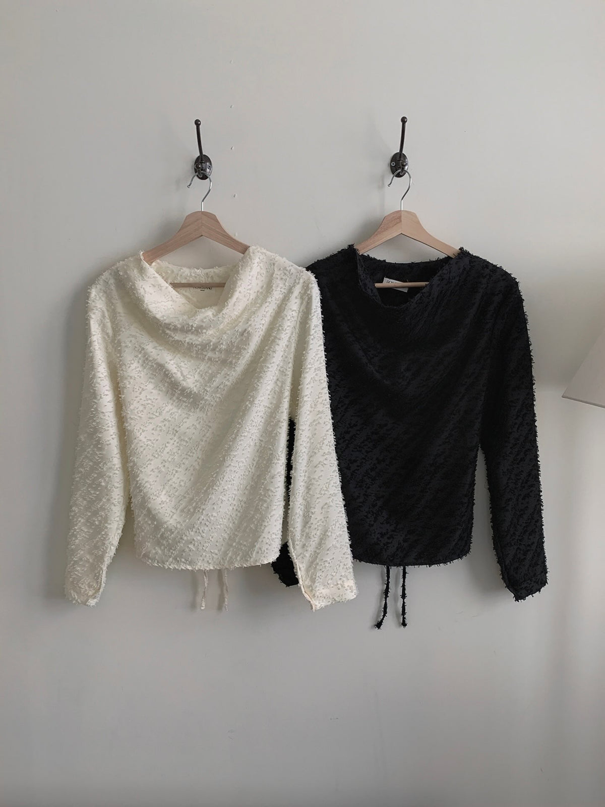 Black and cream textured blouses laid flat with their back waist ties visible.