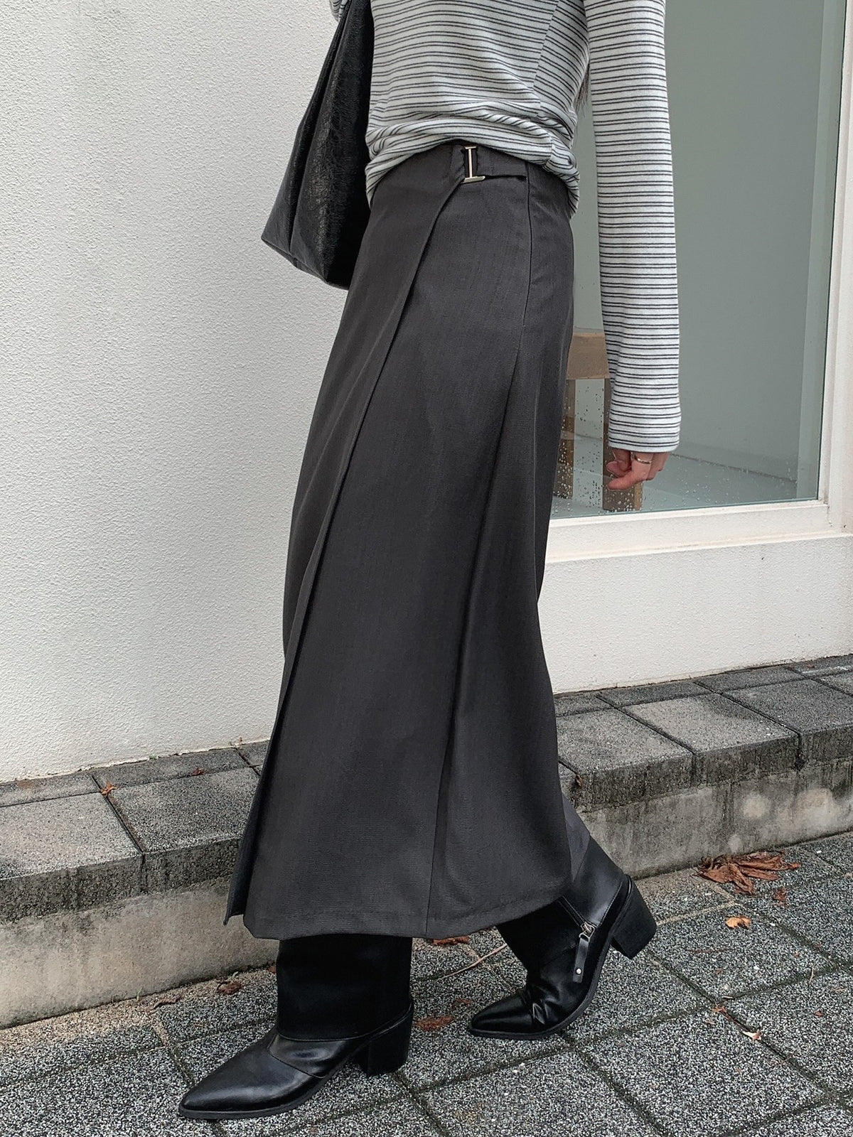 Side view of a charcoal wrap-style midi skirt with a waist buckle, styled with black boots.