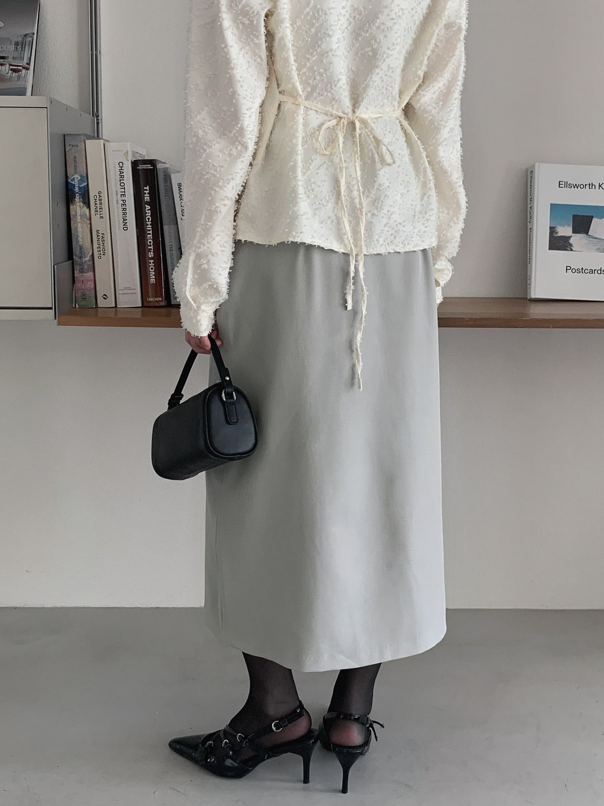 Rear view of a beige midi skirt styled with an ivory tie-back top and black heels.
