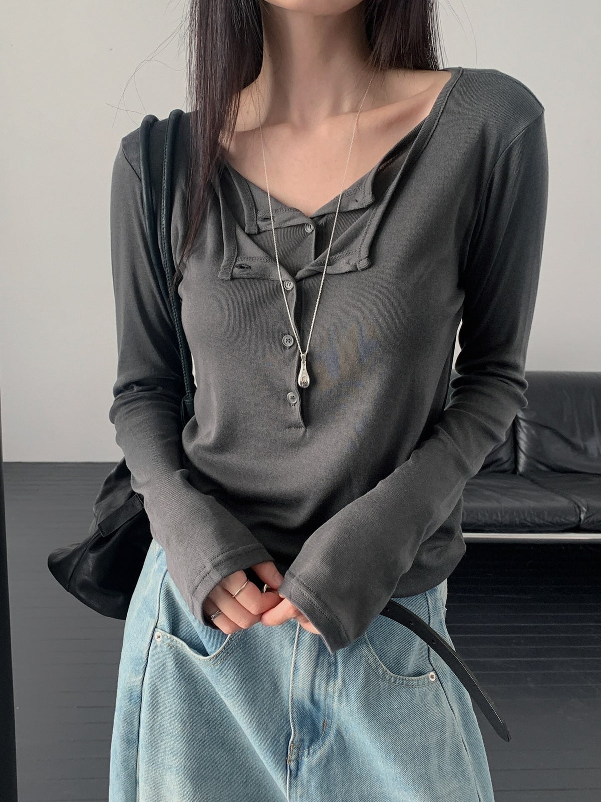 Woman wearing a charcoal long sleeve top with a layered button neckline and light blue jeans.
