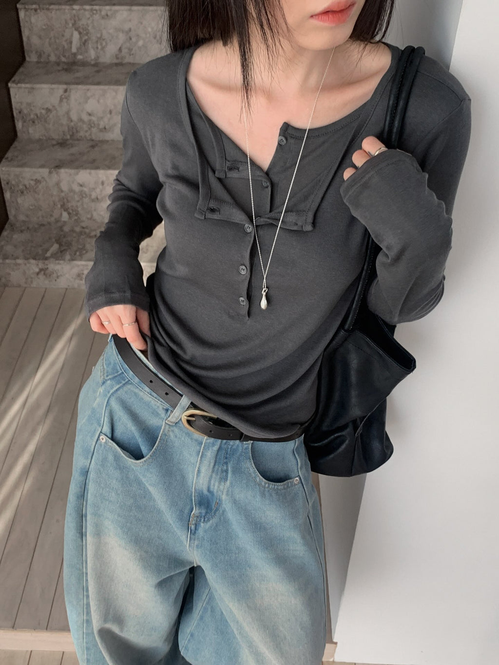 Mirror view of a charcoal button-detail long sleeve top styled with light blue jeans.