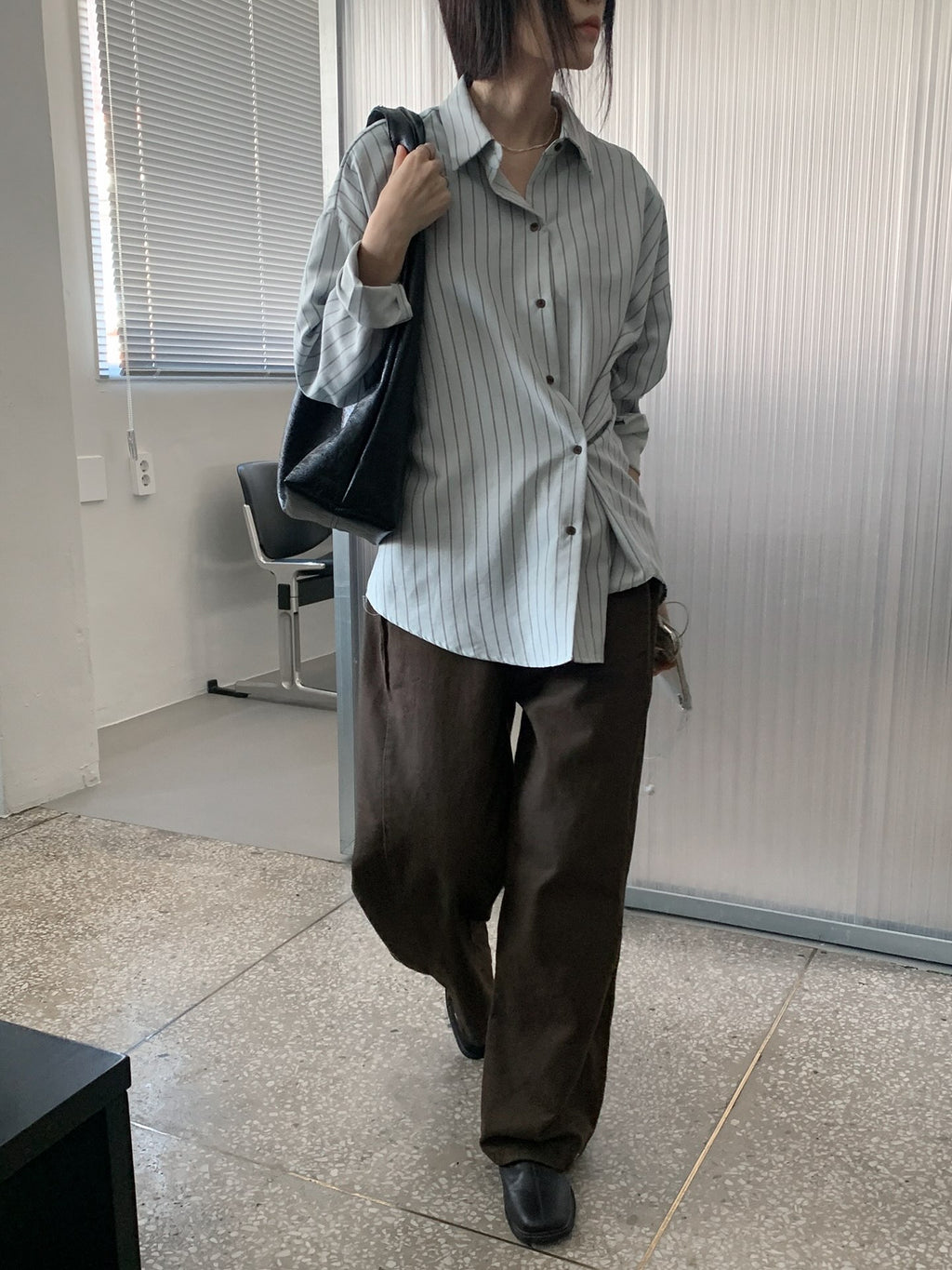 Front view of a woman wearing a sky blue striped shirt with dark trousers.