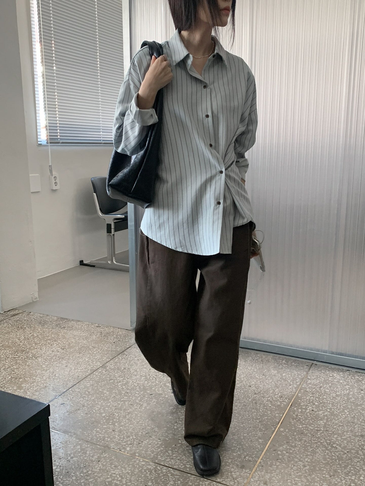 Front view of a woman wearing a sky blue striped shirt with dark trousers.