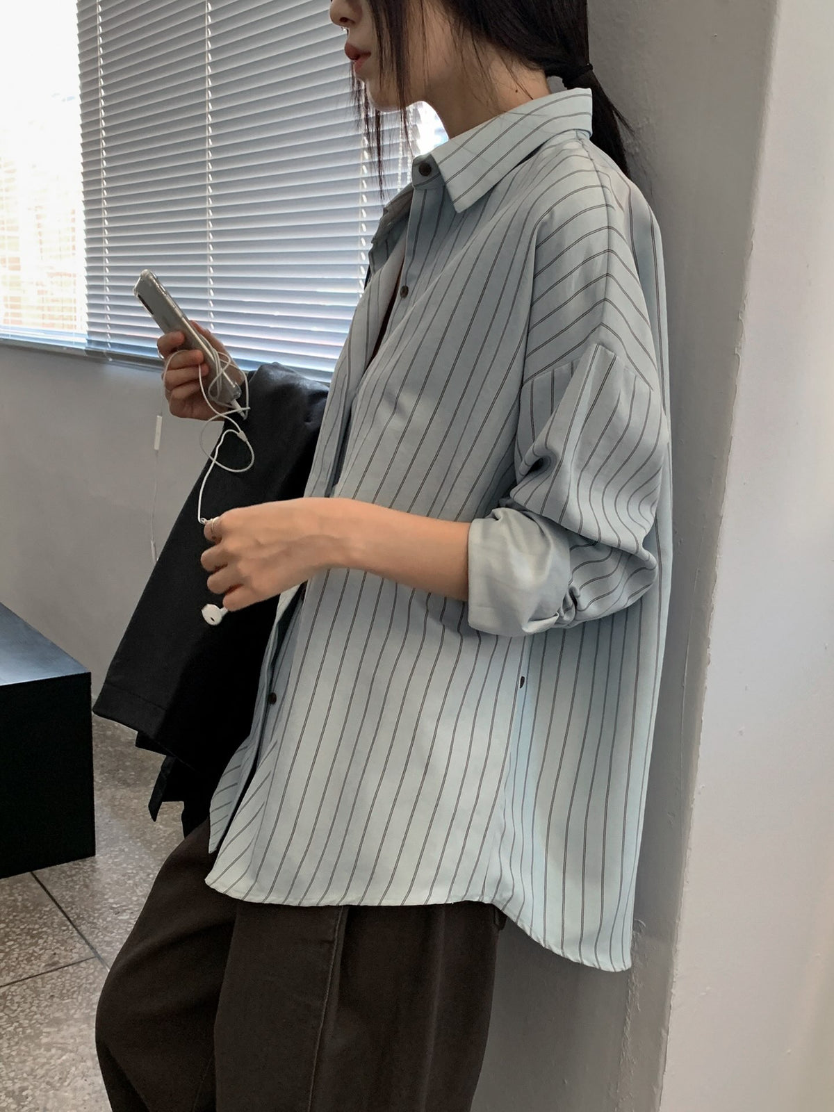 Side view of a sky blue striped shirt showing its collar, sleeve and curved hem.