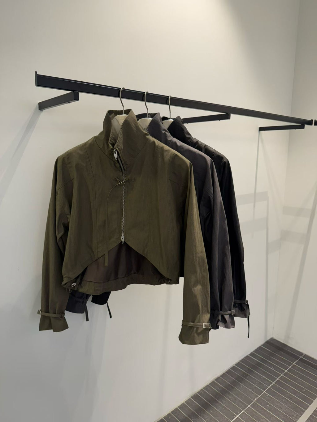 Front view of Khaki, Charcoal and Black zip-up bolero jackets on hangers