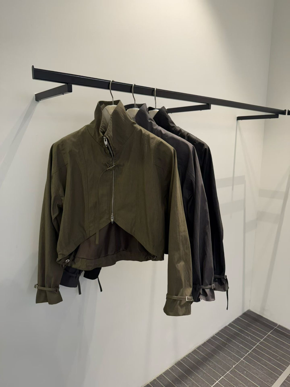 Front view of Khaki, Charcoal and Black zip-up bolero jackets on hangers