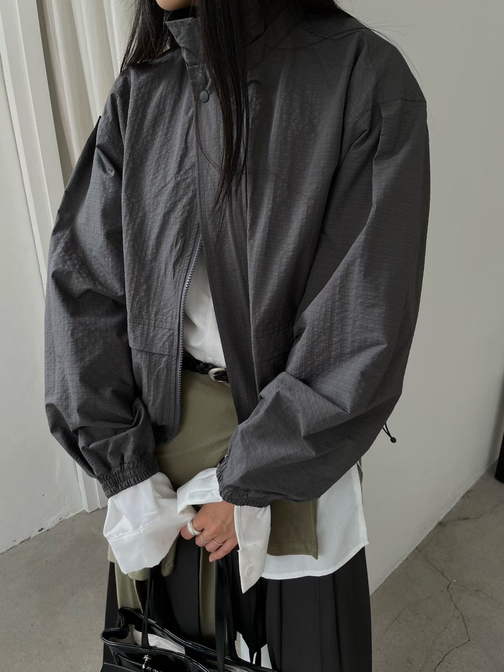 Close-up of charcoal high-neck jacket showing snap placket, zip and elasticated cuffs