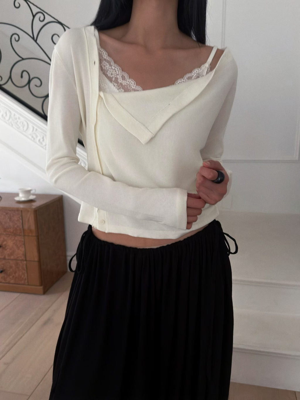 Front view of a black draped button cardigan styled with a grey skirt and black bag.