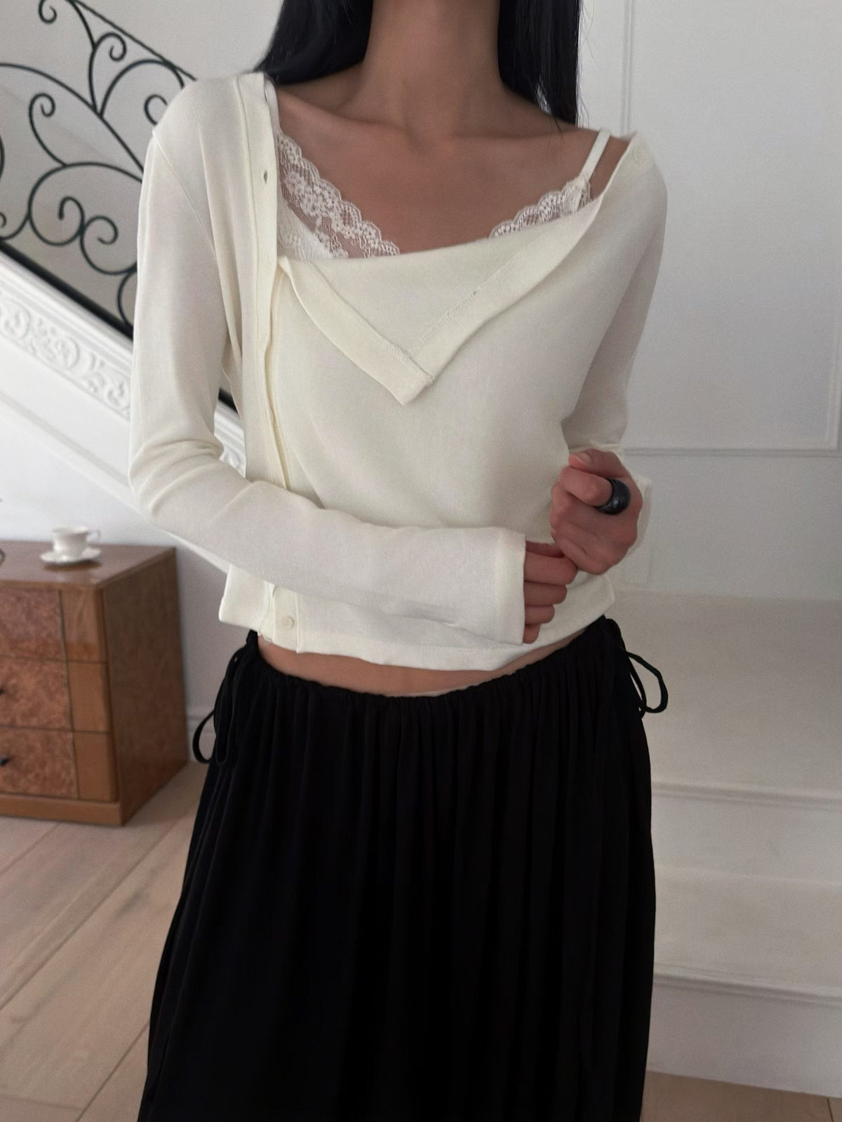 Front view of a black draped button cardigan styled with a grey skirt and black bag.