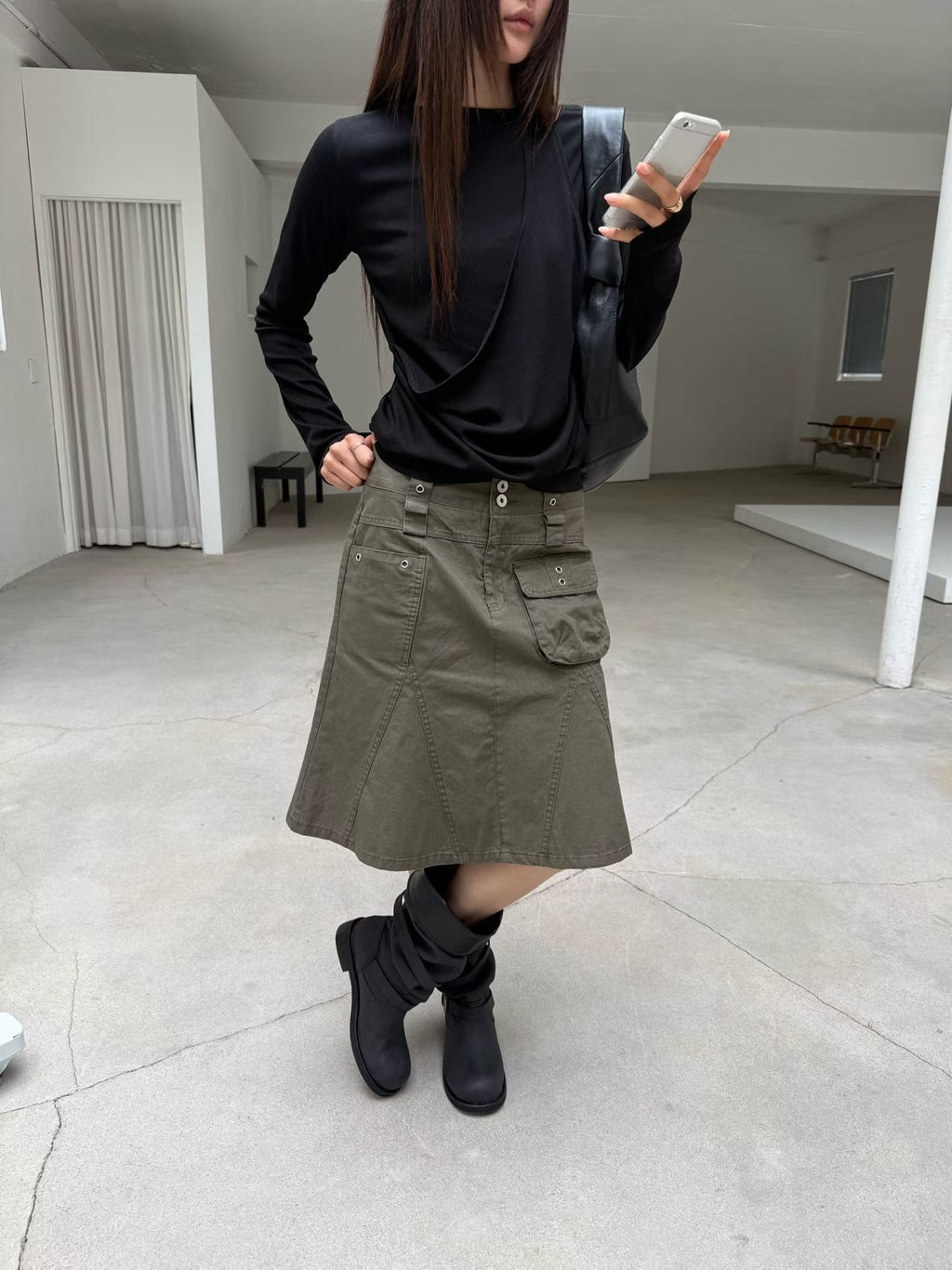 Mirror view of a khaki cargo skirt styled with a black top and black boots.