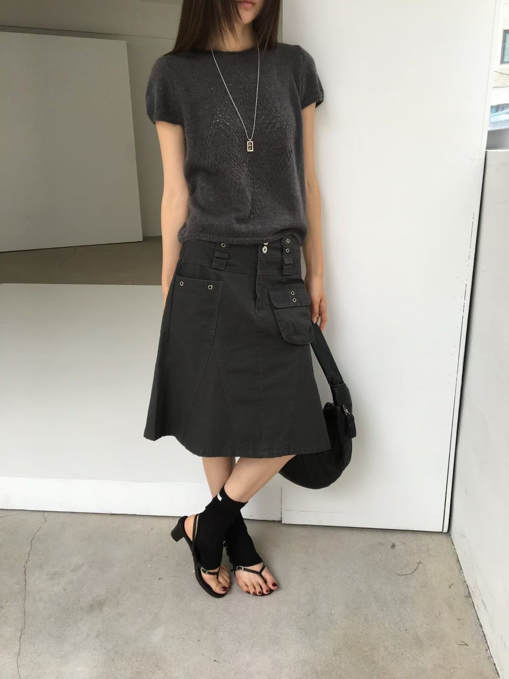 Side close-up of a charcoal cargo skirt showing the patch pocket, eyelets and panel seams.