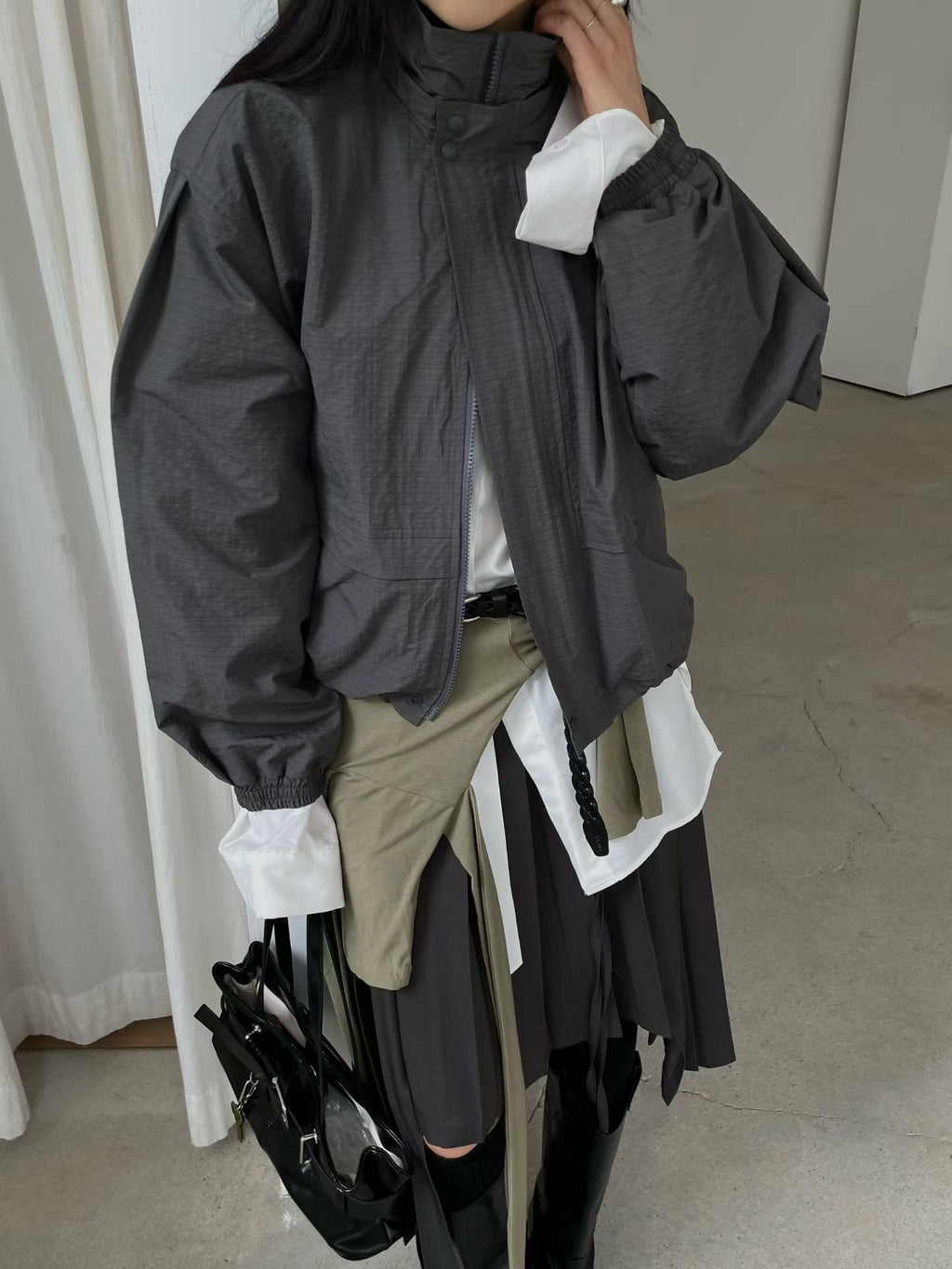 Charcoal high-neck jacket, front detail with raised hand beside the collar