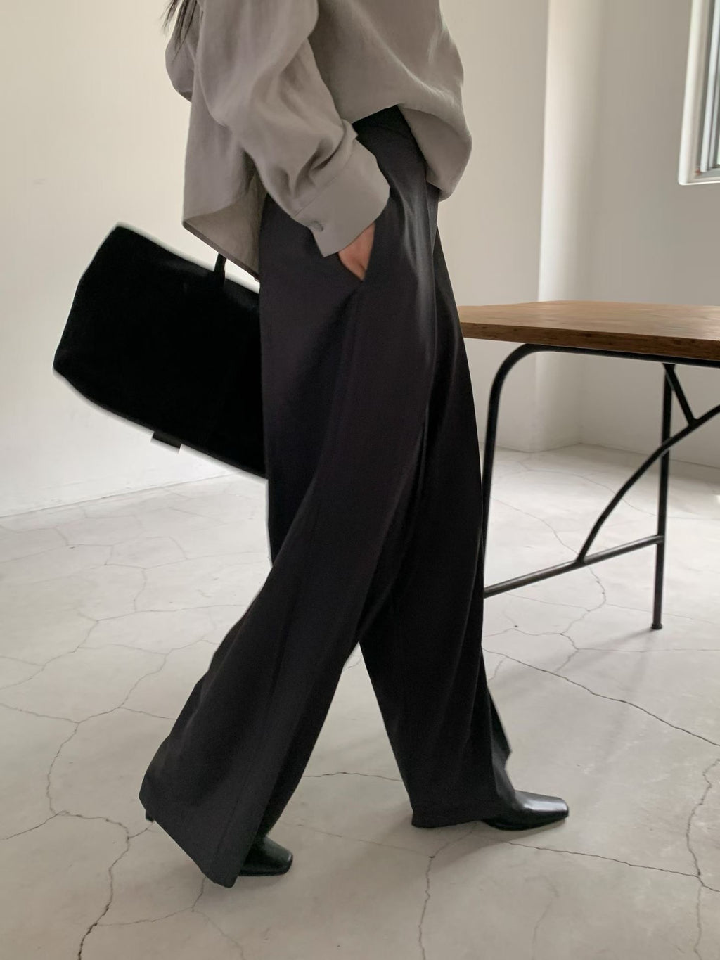 Side view of beige pleated wide leg pants styled with a brown blouse and black shoes.