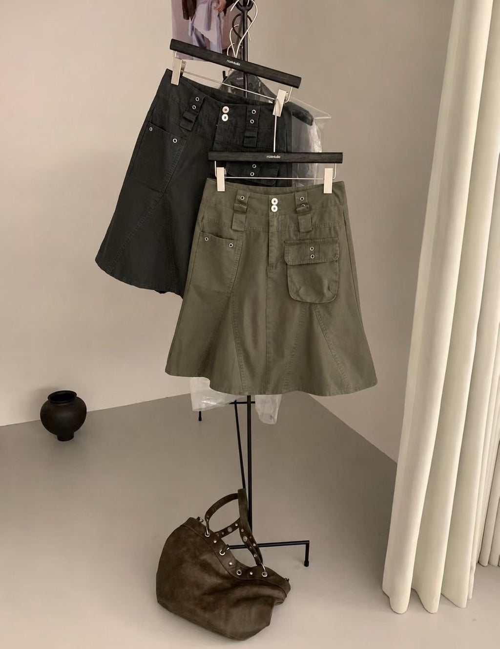 Front detail of a charcoal cargo skirt showing two waistband buttons and asymmetric front pockets.