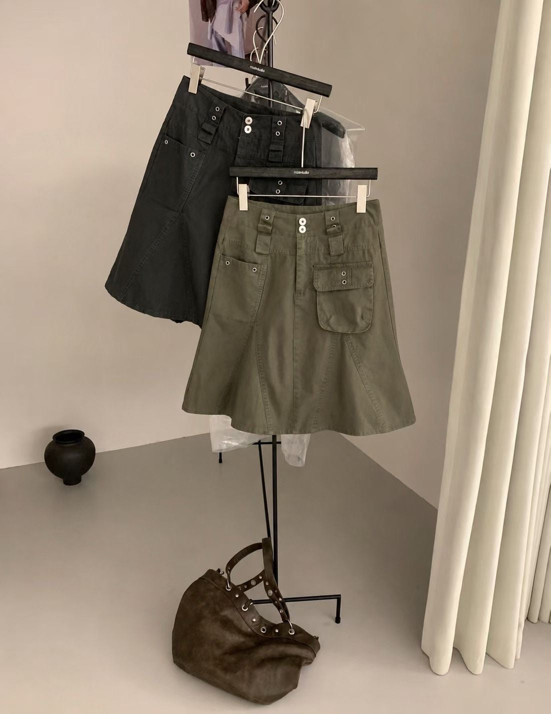 Front detail of a charcoal cargo skirt showing two waistband buttons and asymmetric front pockets.
