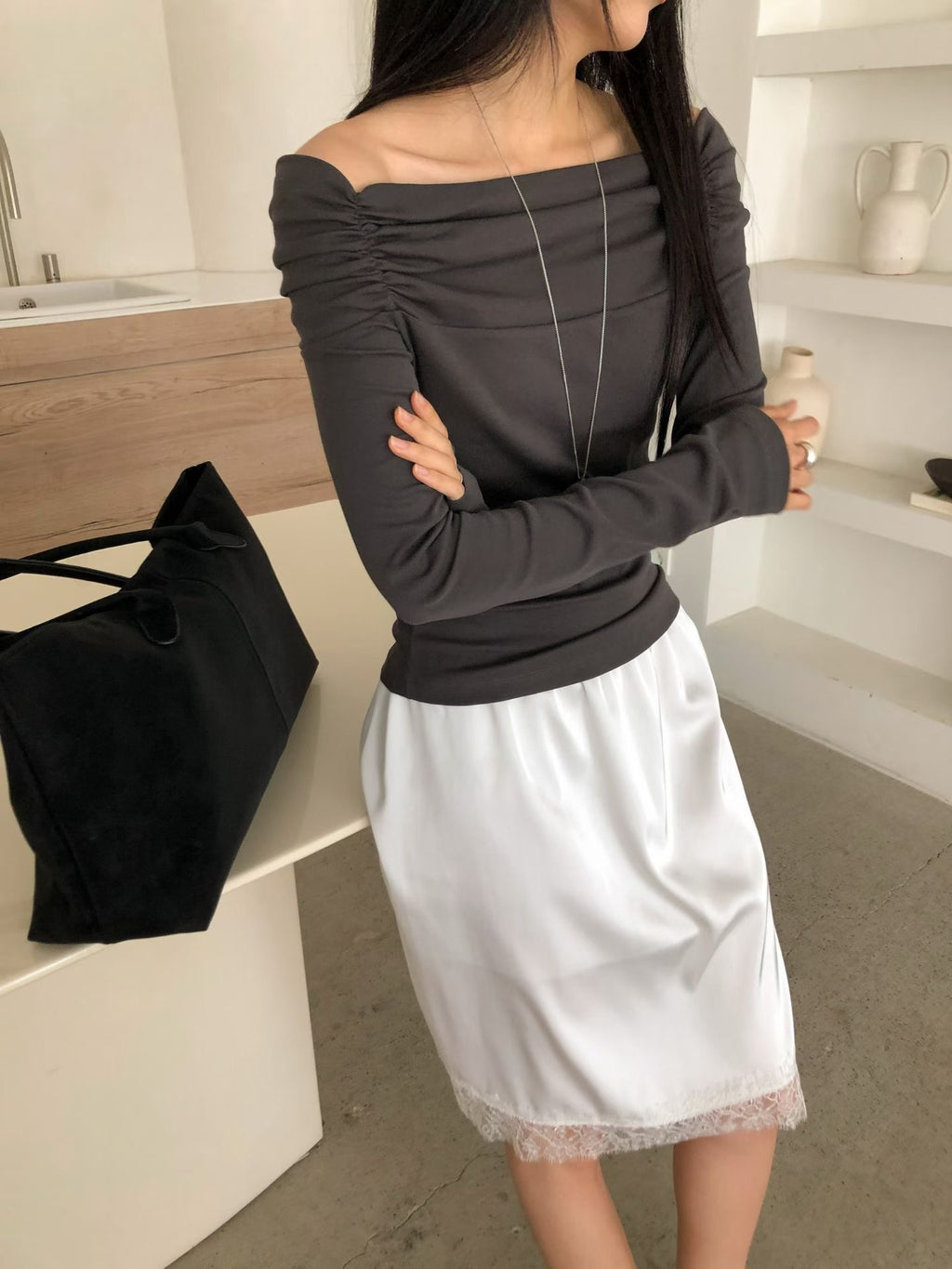 Full-length outfit with a charcoal off-shoulder top, white lace-hem skirt and brown flats.
