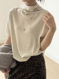 Front detail of an ivory short sleeve mock neck sweater worn with a pendant necklace.