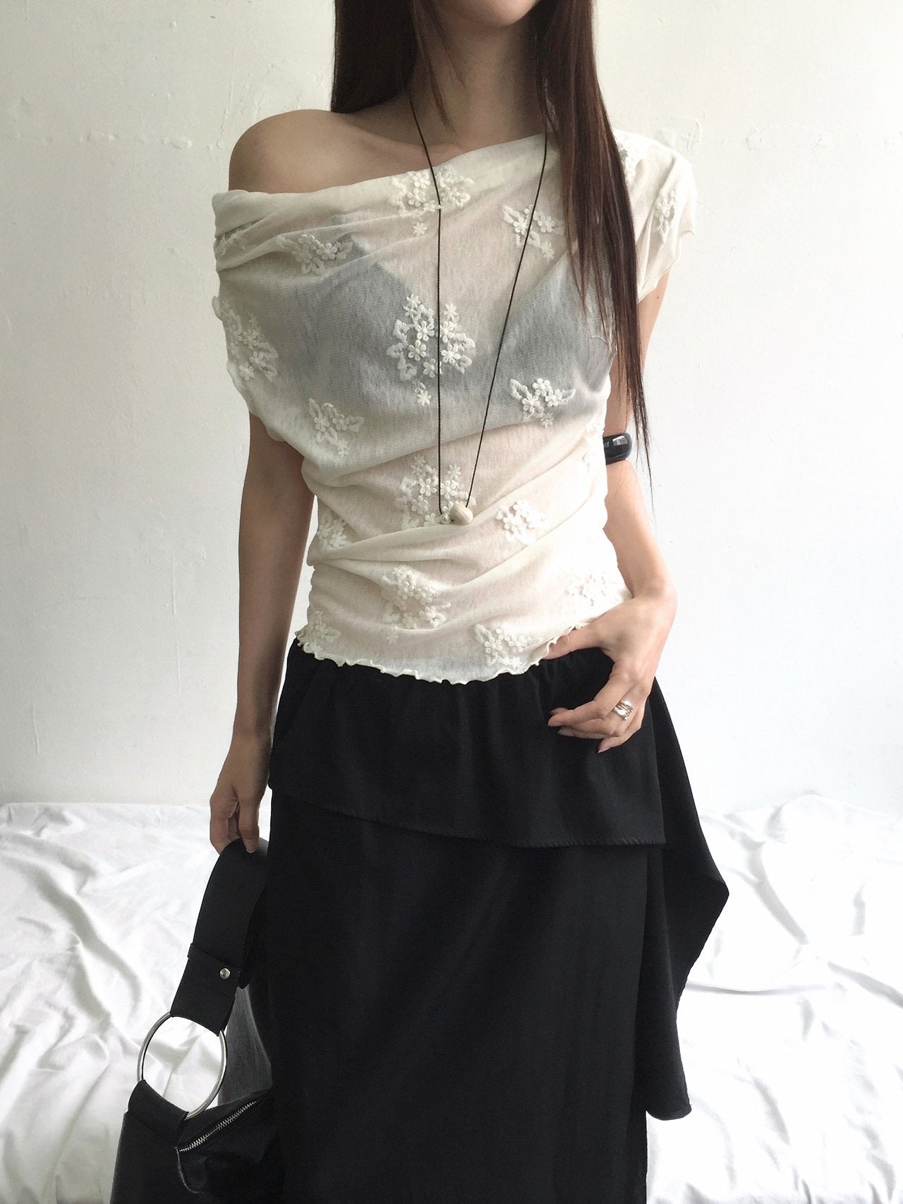 Nweol one-shoulder floral lace mesh top in Black, styled on model seated front view with charcoal skirt
