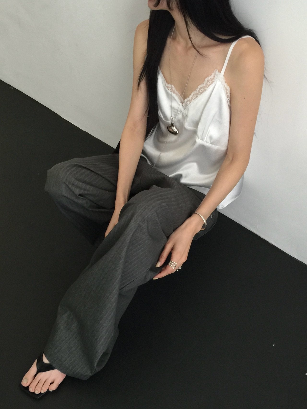Nweol lace trim satin tank top in Ivory, styled on model seated front view with grey wide leg trousers